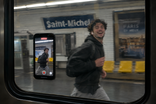 Visuel IA : un téléphone placé contre une vitre de métro filme le quai.