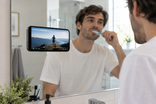 Visuel IA : un homme regarde son téléphone sur un miroir pendant qu’il se brosse les dents.